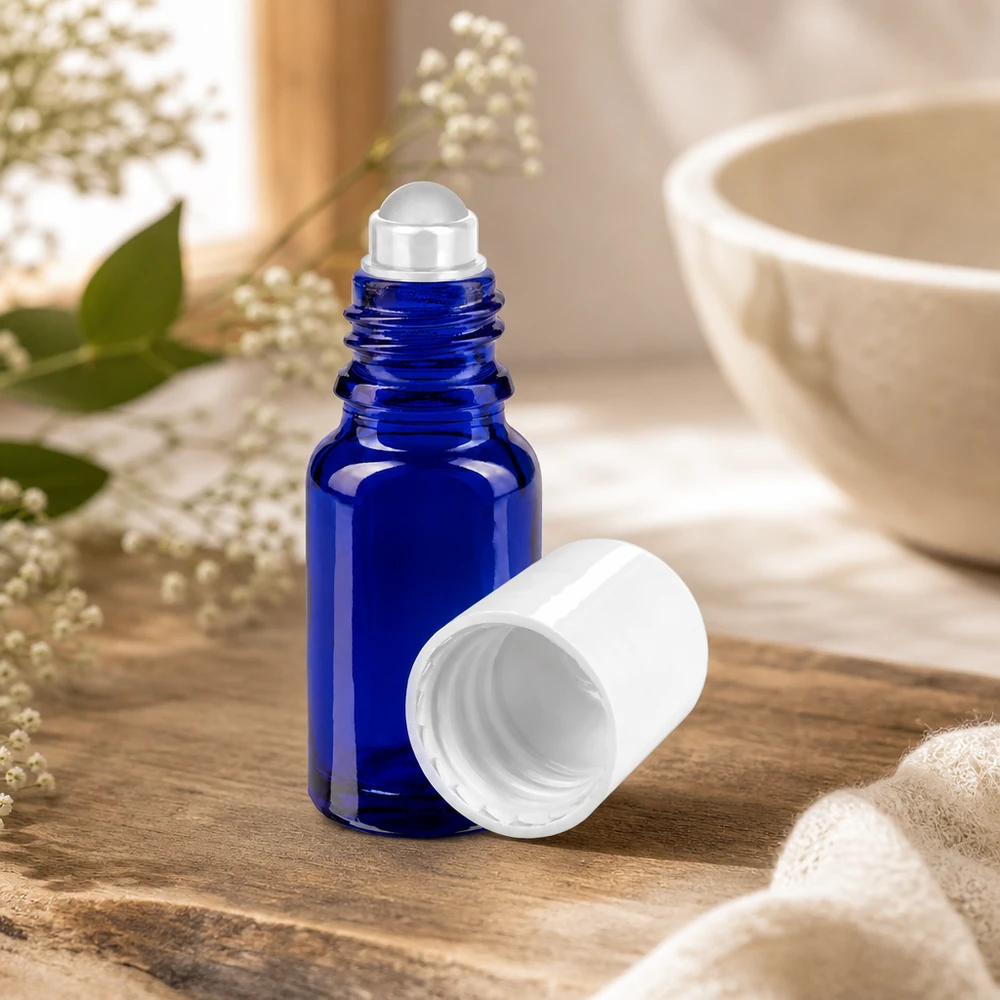 Apothekenflasche blau 10ml Roll-On Verschluss weiß Blaue 10ml Apothekerglasflasche mit Rollapplikator neben Keramikschale und Naturblüten