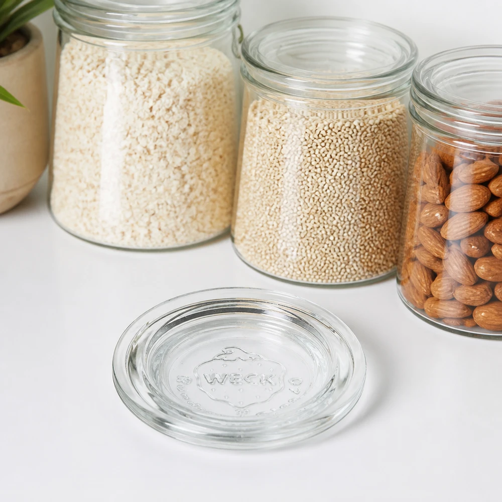 WECK Glasdeckel RR40 transparent vor Vorratsgläsern mit Reis Quinoa und Nüssen auf weißer Arbeitsplatte
