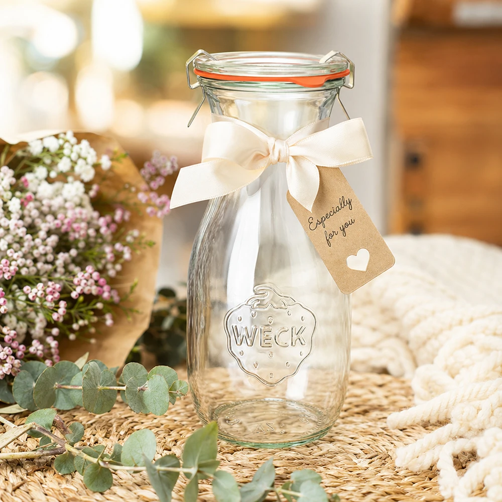 530ml Saftflasche komplett WECK RR60 WECK 530ml Saftflasche RR60 dekorativ mit weißer Schleife und Geschenkanhänger zwischen Blumen arrangiert