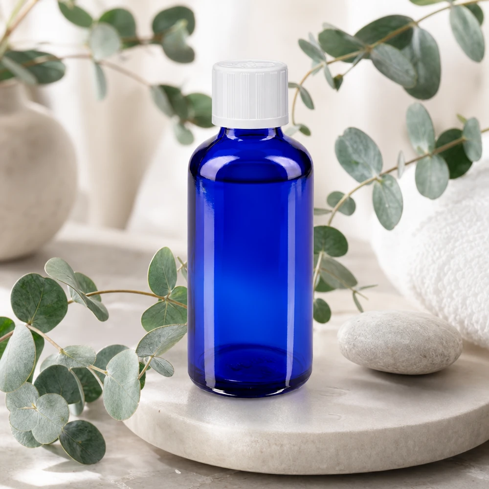 Apothekerglasflasche 50ml kobaltblau mit weißem Verschluss umgeben von Eukalyptuszweigen