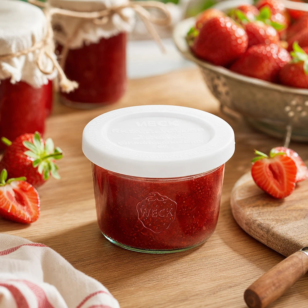 80ml Sturzglas mit Frischedeckel WECK RR60 WECK 80ml Sturzglas RR60 mit Erdbeermarmelade gefüllt auf Holzbrett umgeben von frischen Erdbeeren und Marmeladengläsern