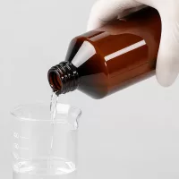 Braune PET Flasche 500ml mit Gewindeverschluss beim Übertragen von Reinflüssigkeit in Becherglas