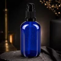 100ml Kosmetikflasche Blau mit schwarzem Pumpspender auf Naturstein vor goldenem Kerzenhalter
