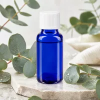 Blaues UV-Schutzglas Apothekerfläschchen 20ml weißer Verschluss umgeben von frischen Eukalyptusblättern