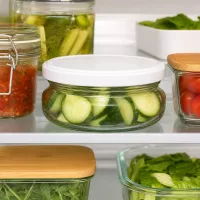 120ml Terrinenglas mit weißem Deckel voller Gurkenscheiben im Kühlschrank neben eingelegtem Gemüse und Konserven