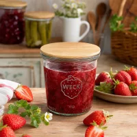 WECK Einmachglas 290ml mit Bambusdeckel gefüllt mit Erdbeermarmelade umgeben von frischen Erdbeeren auf Holztisch