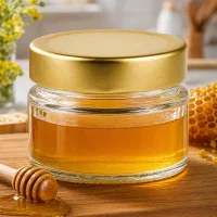 80ml Rundglas mit BasicSeal Deckel gold deep gefüllt mit Honig neben Wabe und Honiglöffel auf Holzbrett