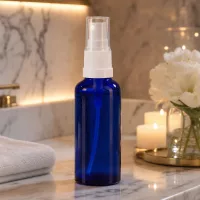 Blaue 30ml Glasflasche mit Pumpsprühkopf in luxuriösem Spa Ambiente mit Frotteetuch und Kerzenlicht