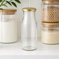 Leere UNiTWIST Glasflasche 150ml mit goldenem BioSeal Verschluss in Küche zwischen Vorratsgläsern mit Lebensmitteln