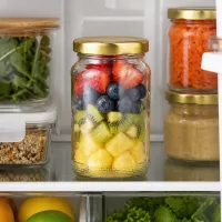 Transparentes 110ml Einmachglas mit buntem Obstsalat und goldenem Twist-Off-Deckel im Kühlschrank