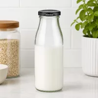 500ml Glasflasche mit Milch gefüllt und schwarzem BioSeal Deckel auf Küchenarbeitsplatte neben Vorratsgläsern