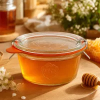 WECK Sturzglas 290ml RR100 mit goldenem Honig gefüllt neben Honiglöffel und Waben als natürliche Aufbewahrung