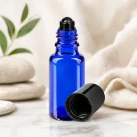 Roll-On Flasche 20ml Blauglas STD schwarze Kappe neben Natursteinen und Textil