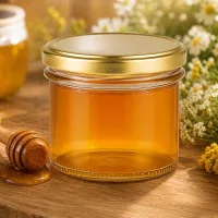 125ml Sturzglas gefüllt mit goldgelbem Honig neben Honiglöffel und Blumen - perfekt für Imkerei und Geschenke