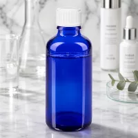 Apothekerflasche 50ml in Kobaltblau mit weißem Schraubdeckel vor elegantem Marmor-Hintergrund