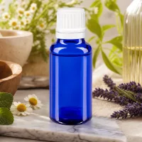 Blaue 20ml Glasflasche mit weißem Tropfsystem auf Marmorunterlage neben Heilpflanzen