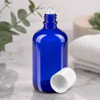 Hochwertige kobaltblaue 100ml Roll-On Flasche aus Apothekerglas vor natürlichem Eukalyptus Hintergrund
