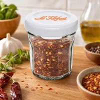 Le Parfait Mini-Sturzglas 44ml mit Chili-Gewürzmischung gefüllt zwischen Kräutern und Gewürzen auf Holzuntergrund