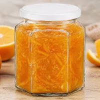 400g Honigglas sechseckig mit Orangenmarmelade gefüllt neben frischen Orangenscheiben auf rustikalem Holzuntergrund