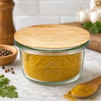 WECK Mini Sturzglas 50ml mit Holzdeckel gefüllt mit gelbem Gewürzpulver in moderner Küche mit Kräutern