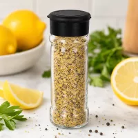 Gefülltes Salz-Streuglas 100ml aus Glas mit schwarzem Deckel neben Zitronenscheiben