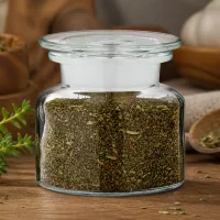 Apothekerflasche Klarglas 100ml mit fein gehackten grünen Kräutern und Knoblauch im Hintergrund