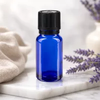 Blaue Tropfflasche 10ml mit OV-Sicherheitsverschluss vor Lavendelzweigen und weißem Keramikgefäß