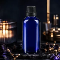 Kleine blaue 50ml Glasflasche mit Dosiertropfer und schwarzem Verschluss auf Schieferplatte mit Blüten