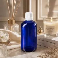 Kleine blaue Glasflasche 100ml mit weißem Sicherheitsdeckel zwischen Kerze und Bambusstäbchen