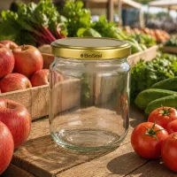 500g BioSeal Honigglas leer mit Golddeckel umgeben von frischen Äpfeln und Tomaten auf Holztisch im Freien