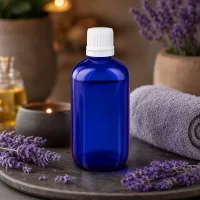 Blaue Medizinglasflasche 100ml mit Dosiertropfer und weißem OV neben Lavendelpflanzen