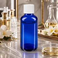 Schlanke 50ml Tropfflasche in Kobaltblau mit weißem Schraubdeckel zwischen Parfümflakons und Blüten