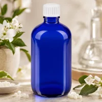 Rundflasche 100ml Blauglas mit weißem Kunststoffdeckel zwischen frischen Blüten und Globuli