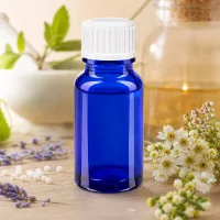Dunkelblaue Apotheker-Glasflasche 10ml mit Schraubdeckel vor natürlichem Kräuterhintergrund