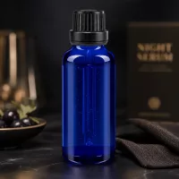 30ml blaue Tropfflasche aus UV-Schutzglas mit schwarzem OV neben dunklen Beeren im Goldschälchen