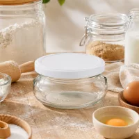 120ml Terrinenglas mit weißem Deckel in Backküche mit Mehl, Eiern und Backzutaten für Dessert-Zubereitung