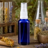 Blaue Apotheker Sprayflasche 30ml STD mit weißem Sprühkopf zwischen Heilpflanzen und Korkgläsern